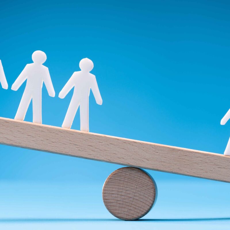 Image demonstrating prioritizing self over social comparison with one person on a balance scale as worth more/tipping the balance versus three on the opposite side